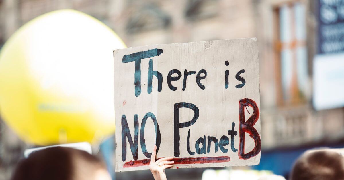 A hand holds a placard with the text: There is NO Planet B